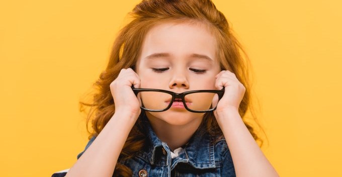 Little girl putting on reading glasses