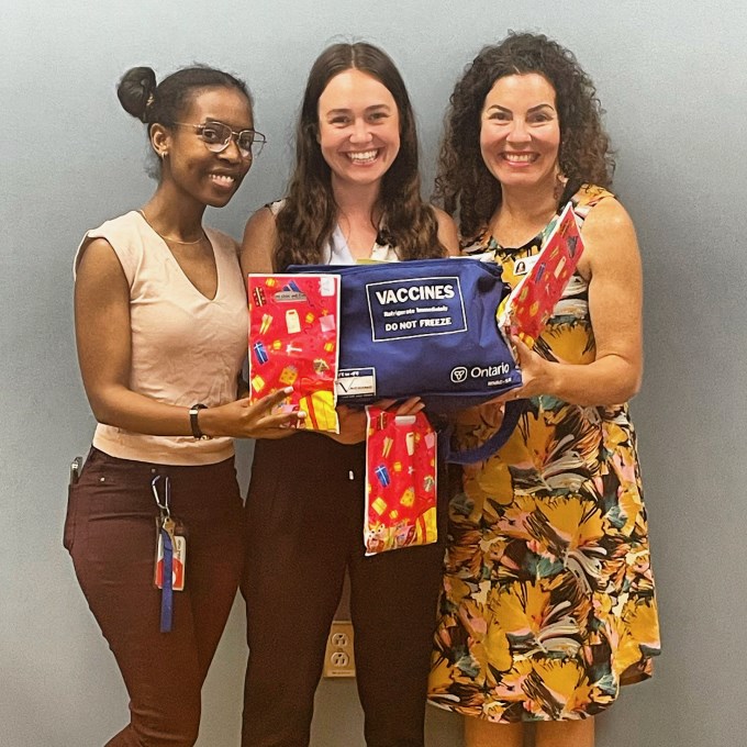 Three smiling women holding a vaccine kit