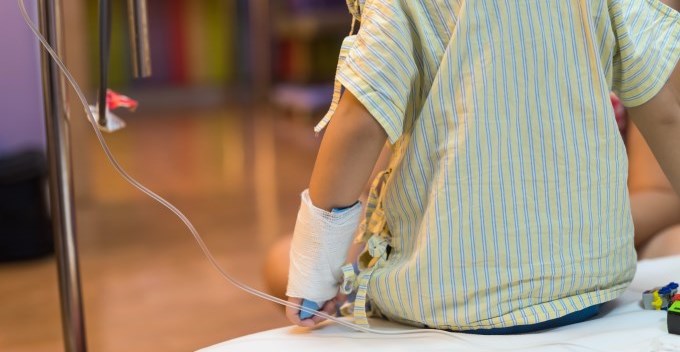 Rear of boy patient sitting on a hospital bed with intravenous